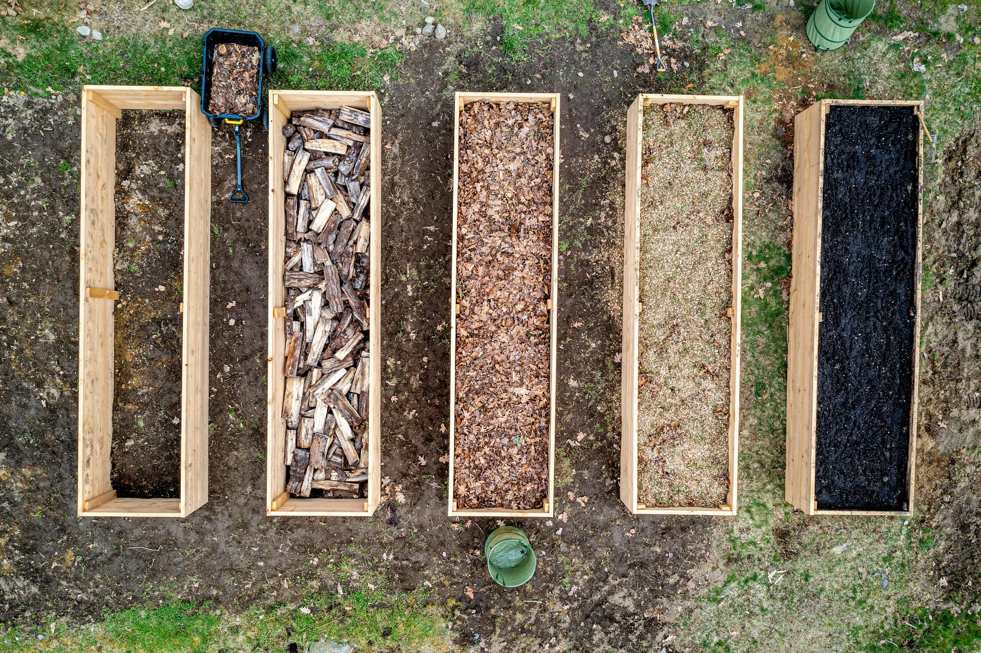 Top view of wooden boxes with piles of firewood wood chips sawdust and coal placed on ground in agricultural plantation